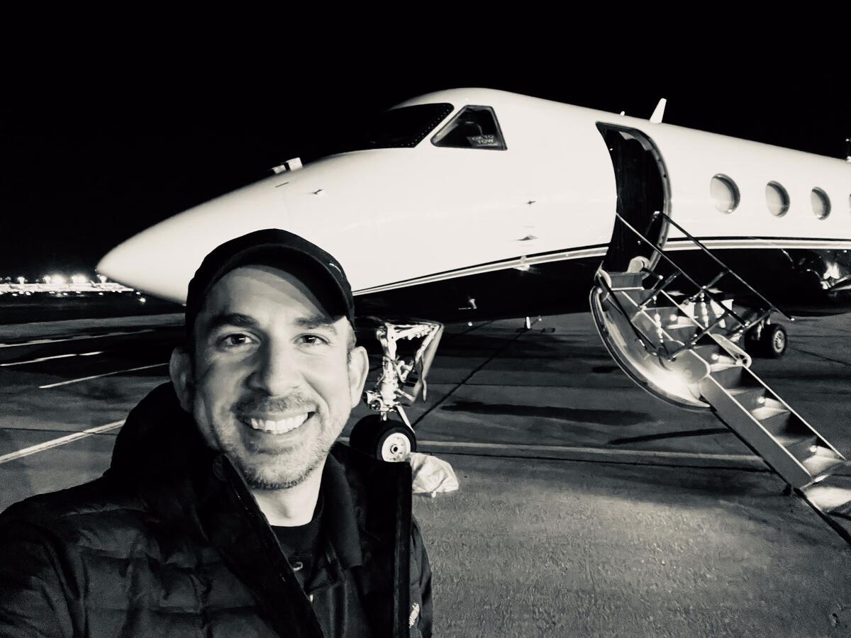 Black and white photo: the studio's owner smiling on a night ramp in front of a business jet with its airstair down